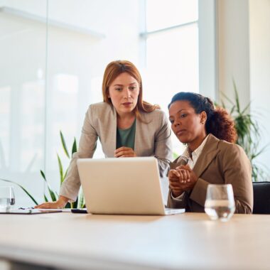 Two businesswomen working together making decisions on a laptop in a modern office