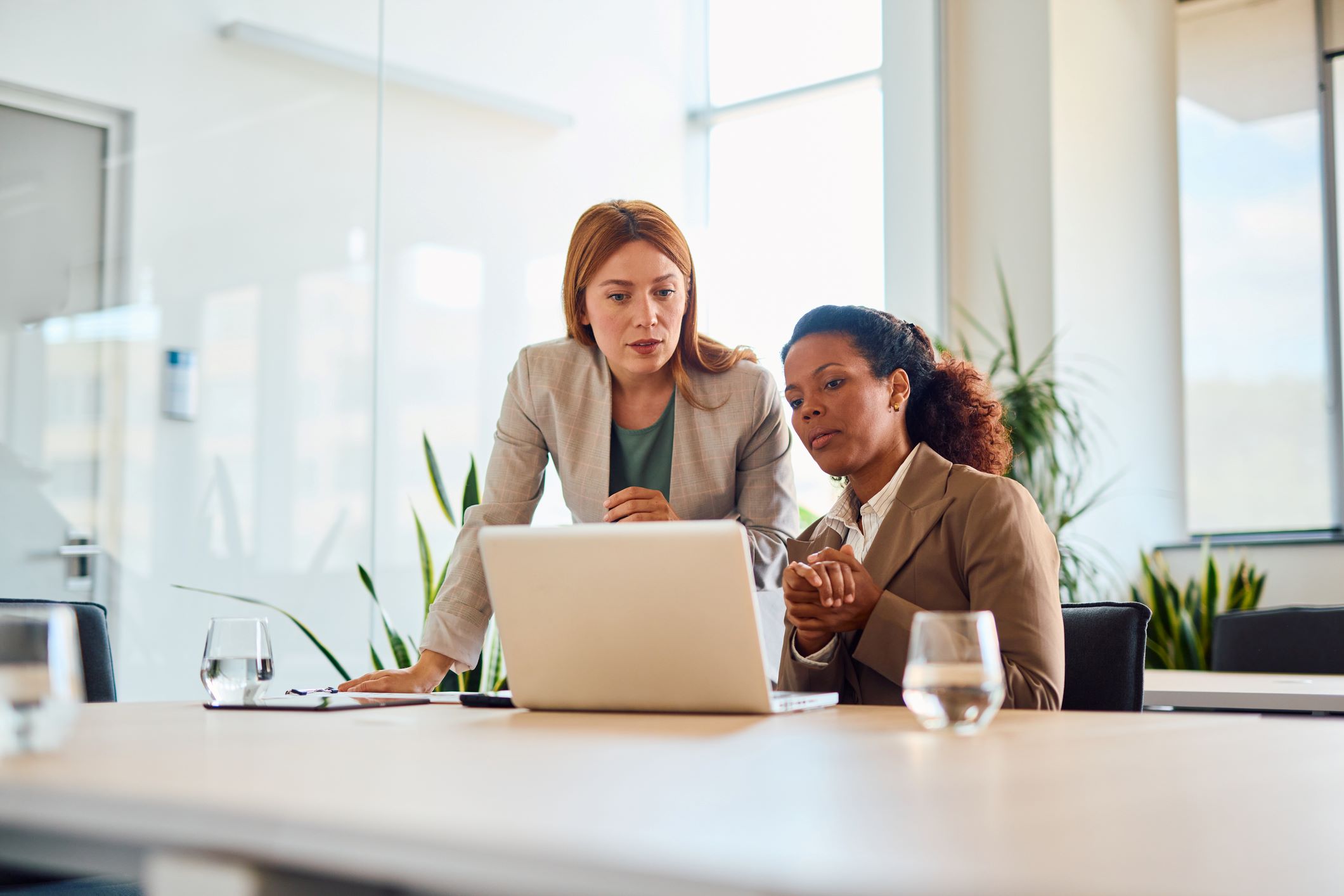 Two businesswomen working together making decisions on a laptop in a modern office