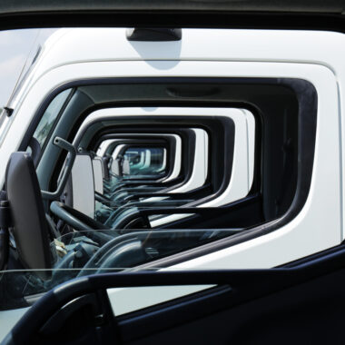 Multiple commercial trucks parked in a fleet yard, viewed through aligned cab windows that create a geometric pattern, symbolising fleet operations, transport and logistics management.