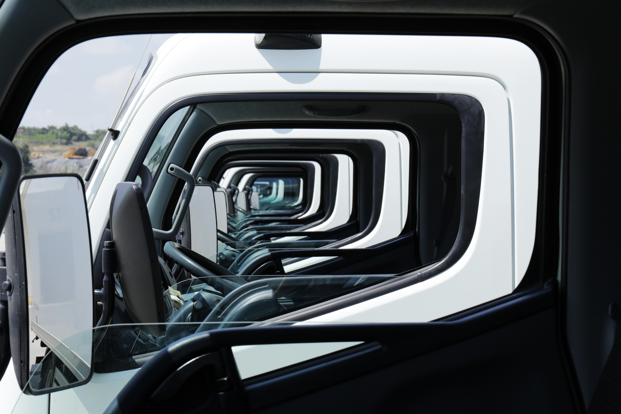 Multiple commercial trucks parked in a fleet yard, viewed through aligned cab windows that create a geometric pattern, symbolising fleet operations, transport and logistics management.